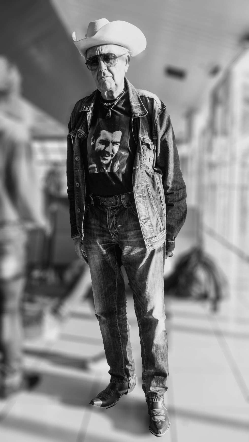 Cuban Messiah: Schwarzweißfoto eines älteren Mannes mit Cowboyhut, Sonnenbrille und Jeansjacke am Flughafen José Martí in Havanna, Kuba