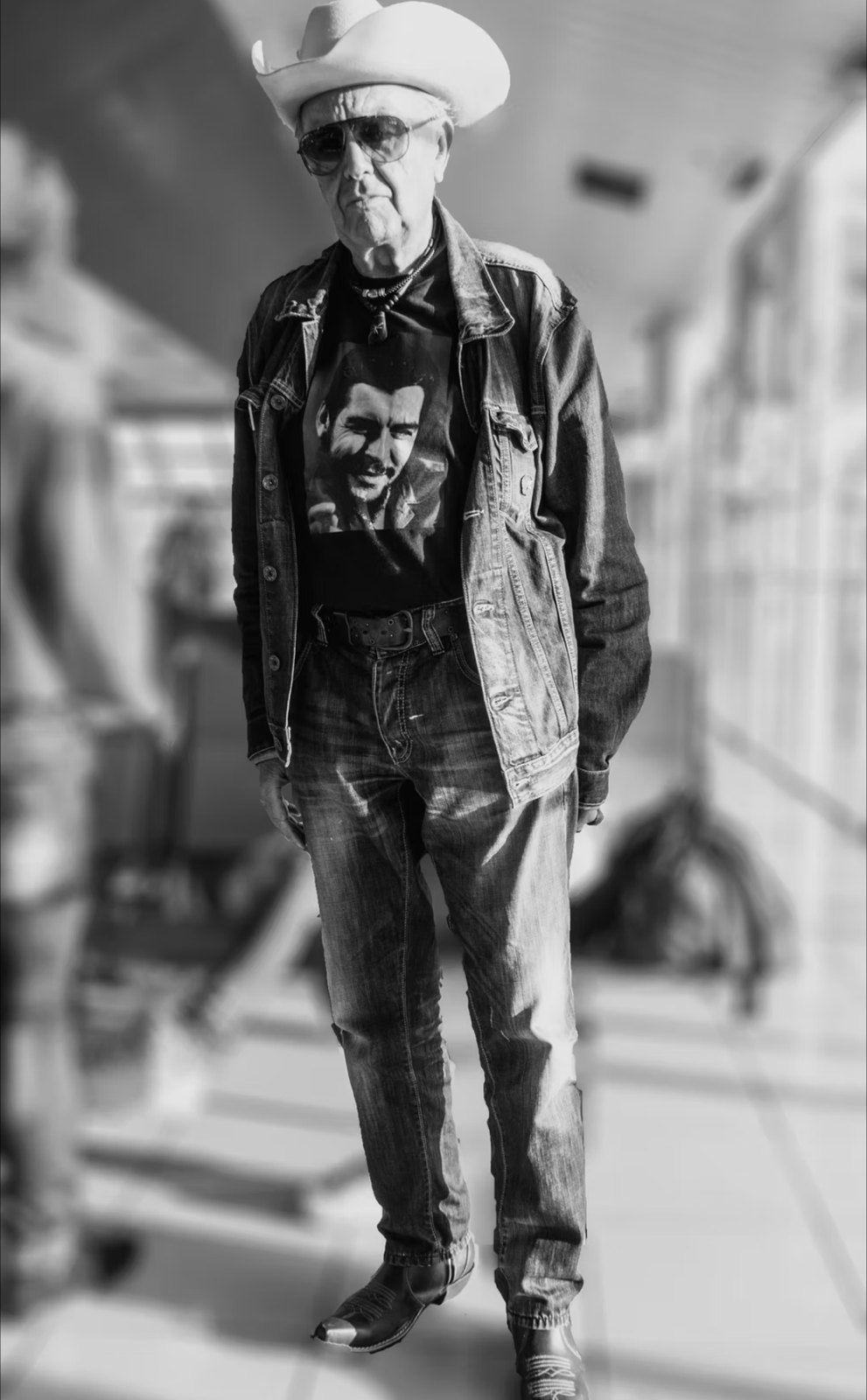 Cuban Messiah: Schwarzweißfoto eines älteren Mannes mit Cowboyhut, Sonnenbrille und Jeansjacke am Flughafen José Martí in Havanna, Kuba
