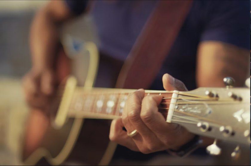 Nahaufnahme von Händen, die Akkorde auf einer Akustikgitarre greifen