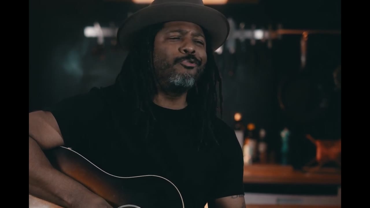 Roger William Smith mit Hut spielt lächelnd Akustikgitarre im Musikvideo Home Cookin'