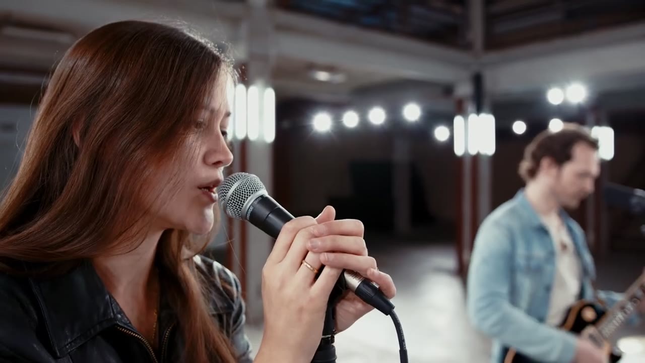 Charlotte Maine singt ins Mikrofon, hinter ihr ihr Gitarrist, im Musikvideo Stay
